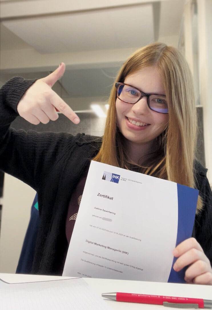 Justine hält ihr Zertifikat der IHK zur "Online Marketing Managerin" in den Händen.